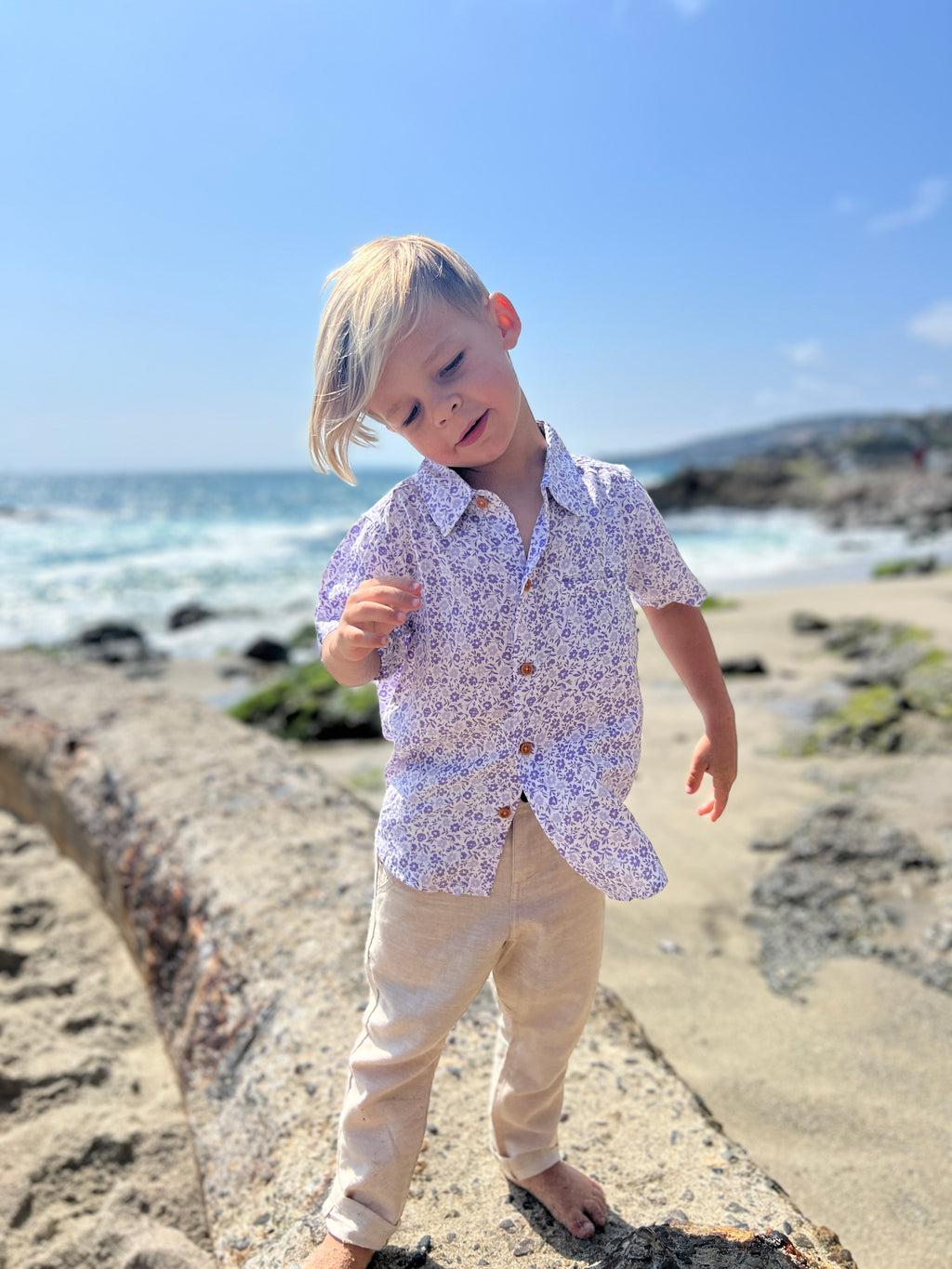 blonde hair boy wearing the lilac floral woven shirt with our beige gauze pants, at the beach