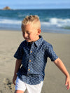 blonde hair boy wearing the chambray anchor woven shirt and white gauze shorts, walking in the sand at the beach in summer. henry.