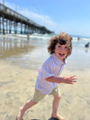 little, boy, running, on, the, beach, stone, twill, shorts, beige, white, short, sleeved, shirt, long, brown, curly, hair, spring, summer, henry,