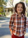 little boy, brown curly hair, wearing rust plaid woven shirt, red twill pants, outside house on pavement, smiling, hands in pockets