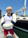 White, Nautical, printed, tee, blonde, hair, red, shorts, boy, holding, a, life, saver, standing, next, to, a, boat, summer, henry.