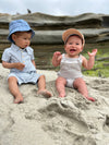 Apricot, woven, cap, beige, bubble, other, little, boy, wearing, navy, heathered, hat, blue, white, polo, romper, button, buttons, siting, in, sand, henry.