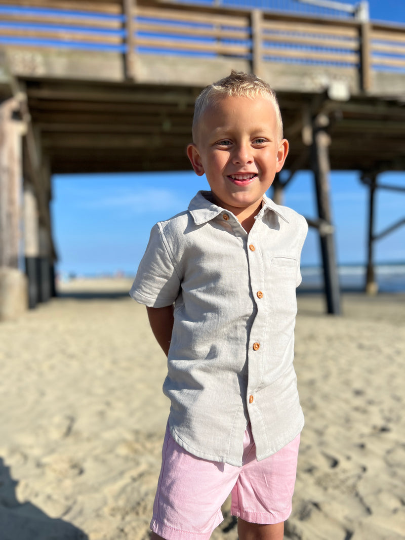 blonde hairy with blue eyes wearing the pale blue woven shirt ad pink twill shorts at the beach