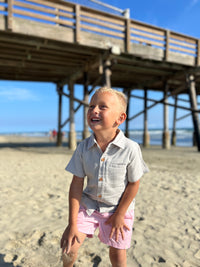 blonde hairy with blue eyes wearing the pale blue woven shirt ad pink twill shorts at the beach