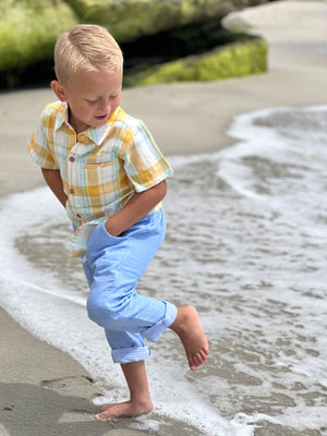 Blonde hair boy with blue eyes, wearing the gold/cream plaid woven shirt and blue heather pants with the leg cuffs folded up, playing in the sea.