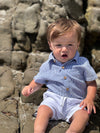 Child in a navy seersucker woven onesie , White shorts sitting on rocks by the beach