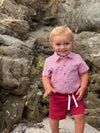 Child in a Red striped woven onesie  and red shorts standing on a rocky beach.