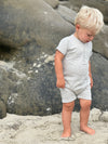 Fair haired boy standing on the sand in a henley grey ribbed romper