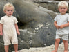 two boys on the beach one wearing beige ribbed romper the other in a white ribbed romper.