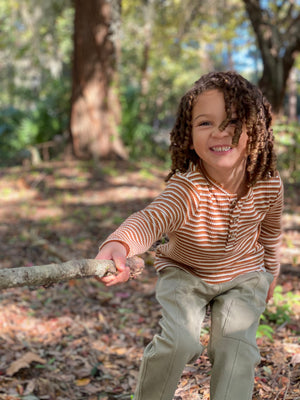 little boy, curly brown hair, beige ribbed henley tee, fern jog pants, playing with stick, in the woodland, autumn leaves on the floor