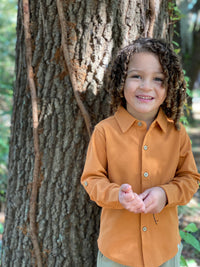 little boy, curly brown hair, pumpkin pique shirt, standing in front of tree,