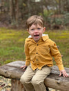 stone twill pants, white drawstrings, straight leg trousers, flexible waistband,cotton, side pockets, black button on waistband, little boy, brown hair,yellow cord hooded woven shirt,s sitting on park wooden bench, woodlands, autumn leaves on the floor, stones, bright day