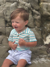 Child wearing a Turquoise striped Jersey onesie and White shorts sitting on rocks.