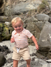 Child in Peach/White striped Jersey onesie Beige shorts standing on a rocky beach
