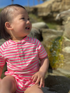 Child in a neon pink and white striped Jersey onesie sitting on rocks.