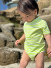 Child wearing a neon acid green and white striped jersey onesie on the sand