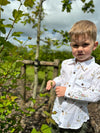 A fair-haired boy stands next to a busy white shirt with an all-over Henry print, featuring buttons and long sleeves, sleeved, sleeve, for a smart look.