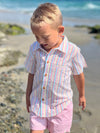 blonde hair boy wearing our candy stripe woven shirt and pink gauze shorts at the beach.