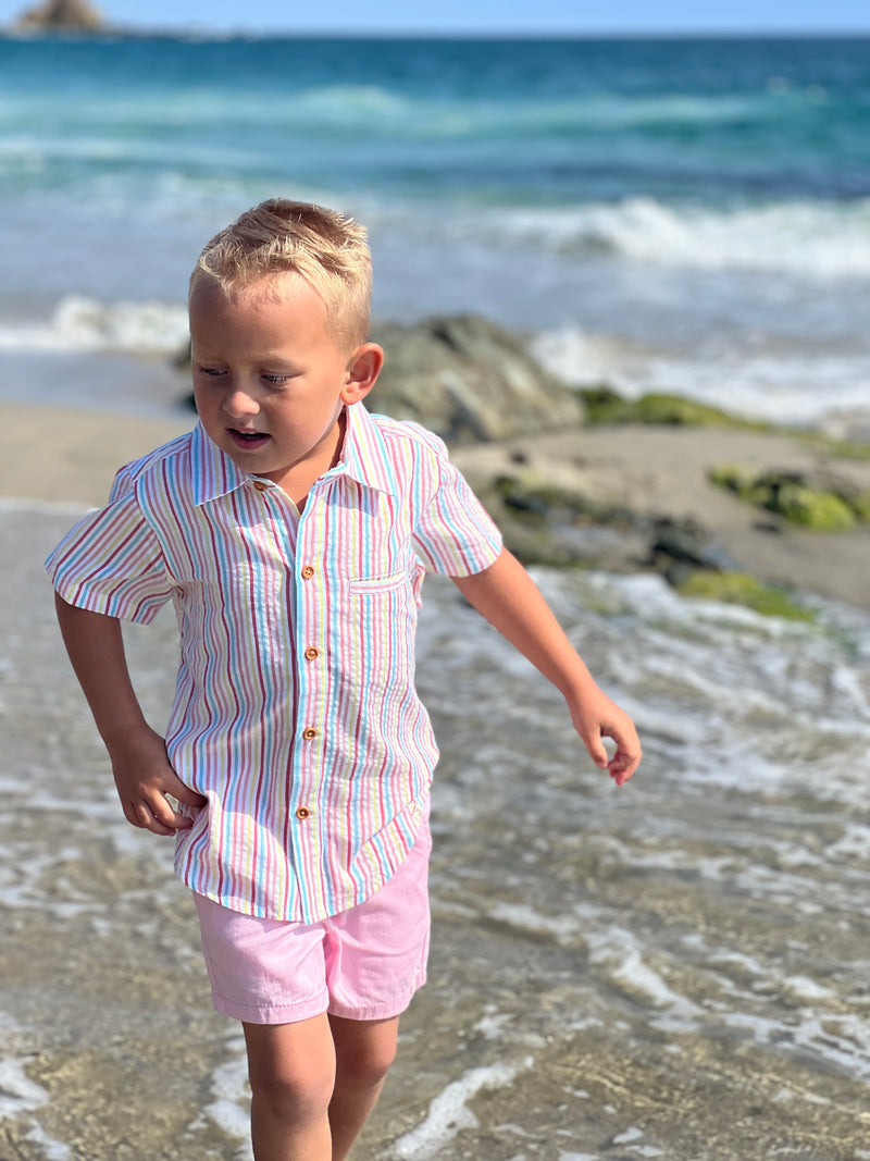 blonde hair boy wearing our candy stripe woven shirt and pink gauze shorts at the beach.