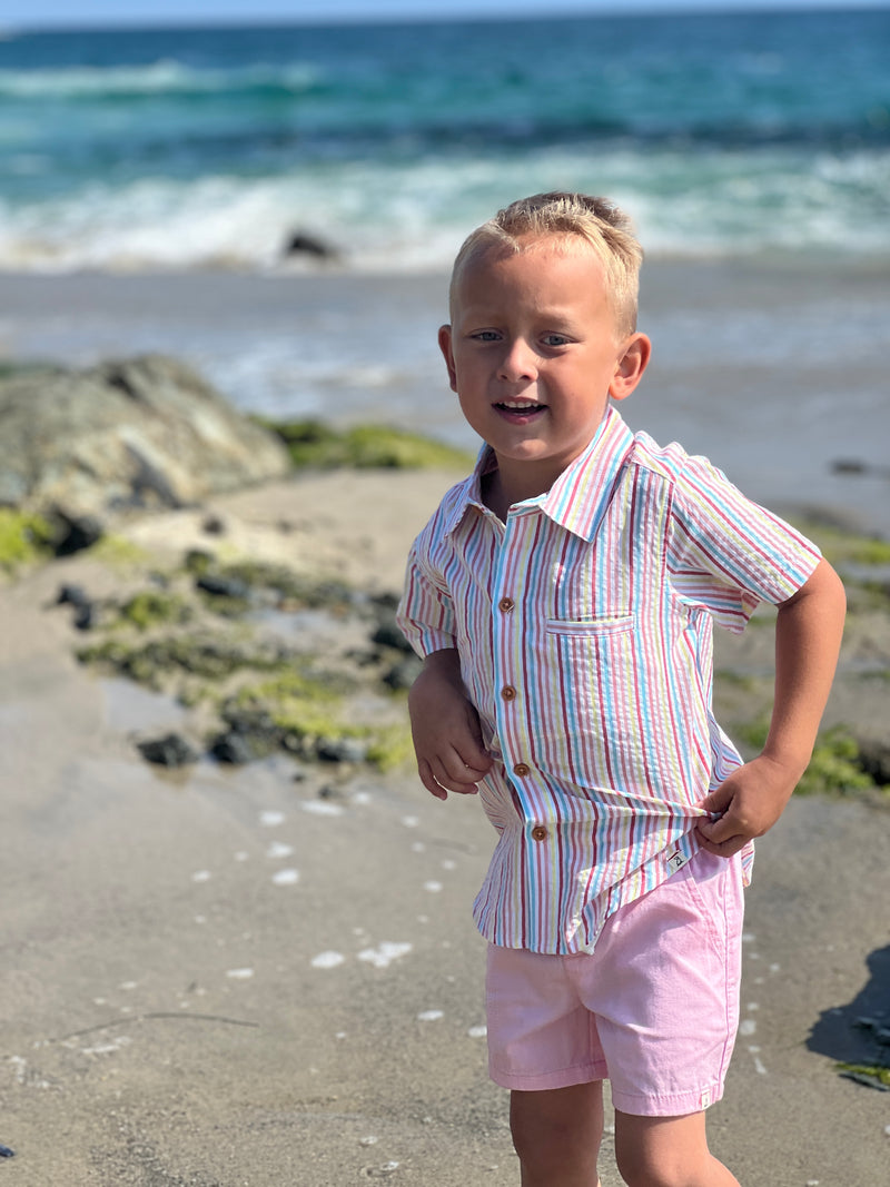 blonde hair boy wearing our candy stripe woven shirt and pink gauze shorts at the beach.