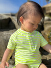 Child wearing a neon acid green and white striped jersey onesie on the sand