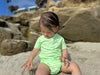 Child wearing a green and white Neon striped jersey onesie sitting on sand