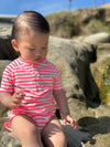 Child in a neon pink and white striped Jersey onesie sitting on rocks.