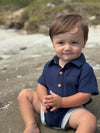 Child wearing a Navy woven onesie sitting on a beach
