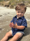 Child wearing a Navy woven onesie sitting on a beach