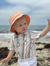 Child wearing a Chambray/Neon striped Woven onesie and Peach Bucket hat, White shorts