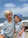 Two children in matching Chambray/mint stripe standing on a beach with ocean waves in the background.
