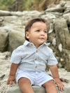 Child sitting on rocks wearing a Chambray Textured woven onesie and white shorts.