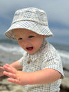 Child wearing a Chambray/cream plaid woven onesie and hat on a beach