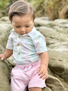 Child sitting on Rocks wearing a Green/Gold striped woven onesie and pink pants